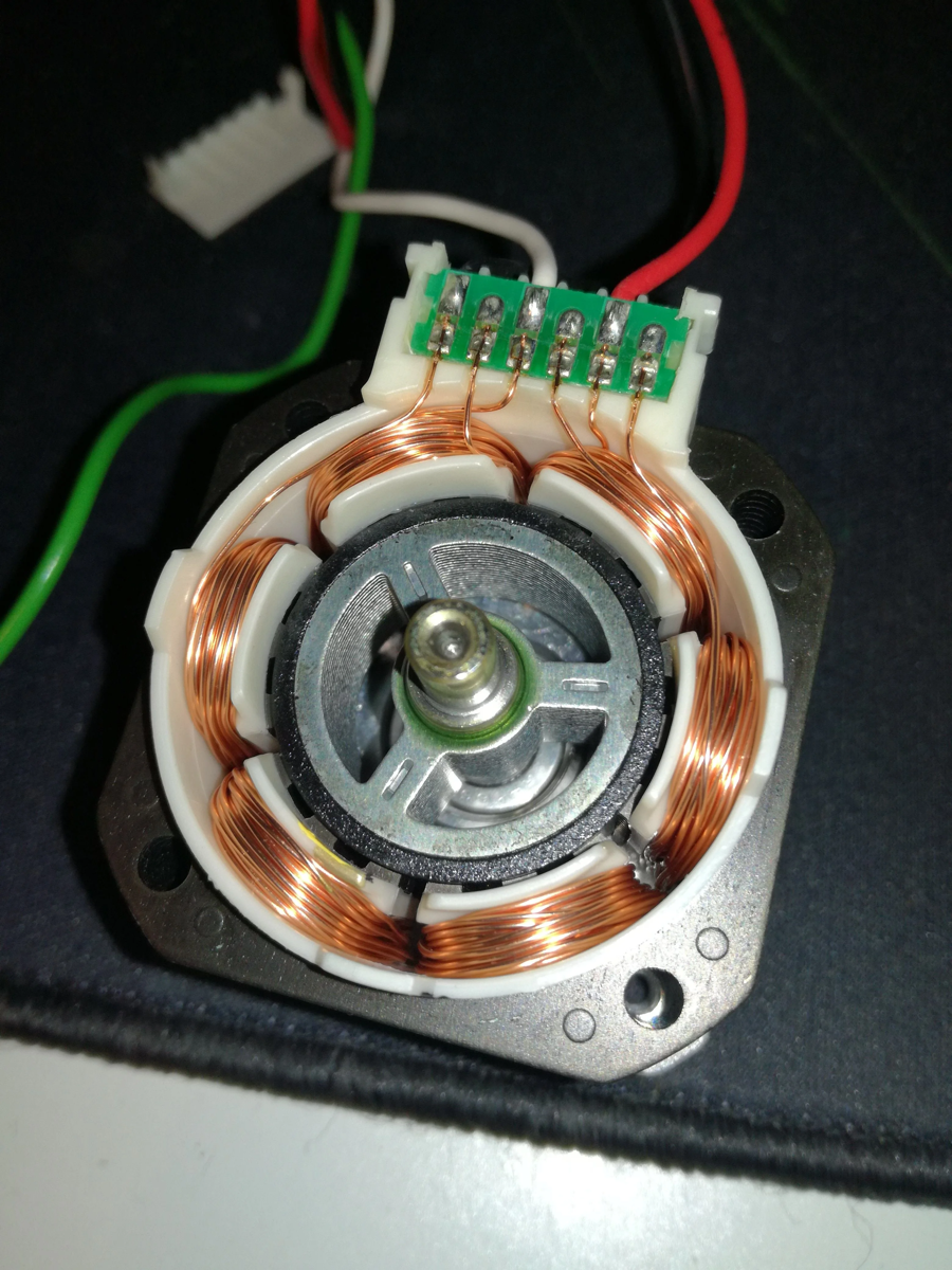 Opened stepper motor exposing the rotor and surrounding copper stator windings connected to colored leads.